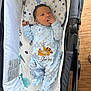 baby, newborn, onesie, blue_clothing, baby_carrier, cushion, simba_embroidery, hand_near_mouth, wooden_floor, stroller, dinosaur_print, star_print, infant, cute, sleepwear, indoor, portrait, cozy, child, relaxing