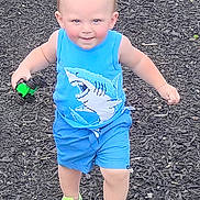 Kian is registered to the contest to win money with this photo: toddler, child, outdoor, playground, toy_car, blue_clothing, shark_design, green_shoes, mulch_ground, smiling, walking, person, young_child, summer_clothes, happy, active, cute, daylight, casual, fun