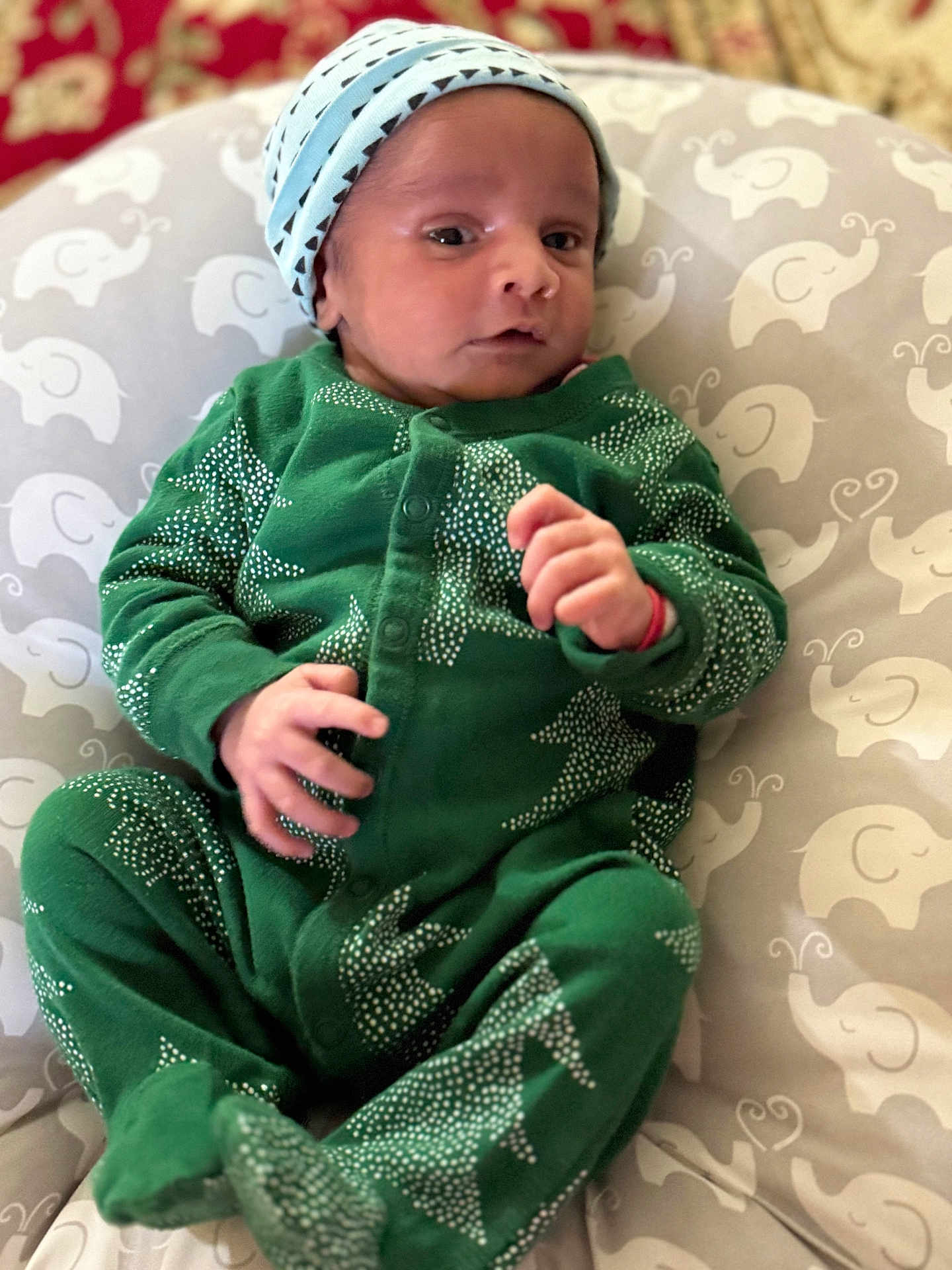 Nirvaan is registered to the contest to win money with this photo: baby, infant, child, green_onesie, hat, cushion, elephant_pattern, indoor, portrait, newborn, cute, clothing, sleepwear, lying_down, small_hands, soft_fabric, face, headwear, baby_bed, resting