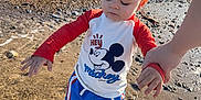 Brooklyn is registered to the contest to win money with this photo: barefoot, beach, child, clothing, holding_hand, mickey_mouse, nature, outdoor, person, rocks, sand, shirt, shoreline, shorts, sky, summer, sunny, toddler, water, waves