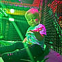 toddler, child, indoor, play_area, netting, colorful_lighting, green_light, pink_light, donald_duck, tshirt, socks, curious, sitting, young_child, portrait, casual_clothing, soft_lighting, expression, hand, playground