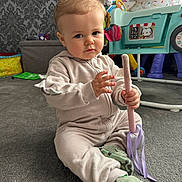 Brooklyn is registered to the contest to win money with this photo: toddler, child, indoors, carpet, toy, wand, ribbons, onesie, shoes, camo, sitting, face, person, play, colorful, background, wallpaper, furniture, expression, floor