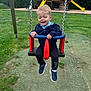 toddler, child, swing, playground, grass, smile, happy, outdoor, play_structure, slide, wooden, blue_jacket, sneakers, casual_clothing, daytime, fun, recreation, park, nature, young_child