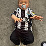 toddler, child, pacifier, carpet, black_and_white_jersey, soccer_jersey, sneakers, reaching_hands, indoor, cute, baby, clothing, footwear, person, young_child, casual_wear, sportswear, floor, lying_down, expression