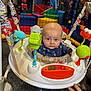 baby, infant, jumper, toys, indoor_play_area, colorful, hand, rings, carpet, plastic, seat, child, face, clothing, blue_outfit, play_equipment, expression, looking_at_camera, netting, soft_toys