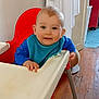 baby, blue_bib, child, clothing, cute, face, feeding, furniture, happy, high_chair, home, indoor, infant, kitchen, person, portrait, red_chair, smiling, wooden_floor, young_child