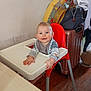baby, bib, child, clothing, face, floor, hands, happy, high_chair, home, indoor, inflatable_ring, person, plastic, red_chair, smiling, suitcase, table, wall, wood_floor