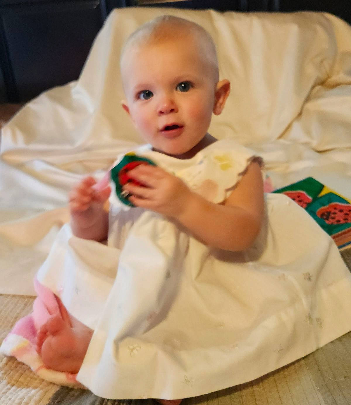 Chloe is registered to the contest to win money with this photo: baby, baby_toddler_clothing, cheek, child, collar, comfort, dress, eye, face, finger, flooring, gesture, happy, iris, linens, person, sitting, skin, sleeve, toddler