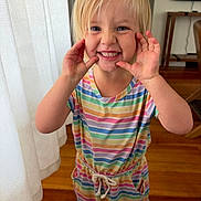 Madelynn is registered to the contest to win money with this photo: child, blonde_hair, striped_dress, rainbow_colors, smiling, playful, indoor, wooden_floor, curtain, furniture, person, happy, cute, portrait, toddler, hands, face, blue_eyes, casual_clothing, home