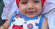 Aslan joined the competition — help win amazing prizes! baby, child, smiling, headscarf, red_clothing, blue_trim, car_pattern, toddler, cute, portrait, face, happy, infant, clothing, fabric, textile, closeup, person, sitting, blanket