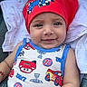 baby, child, smiling, headscarf, red_clothing, blue_trim, car_pattern, toddler, cute, portrait, face, happy, infant, clothing, fabric, textile, closeup, person, sitting, blanket