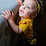 Brooklynn is registered to the contest to win money with this photo: child, toddler, blue_eyes, yellow_clothing, sunflower, headband, curly_hair, smiling, indoor, couch, hand, face, portrait, cute, baby, light, texture, clothing, person, expression