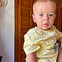 toddler, child, boy, blue_eyes, yellow_shirt, indoor, wooden_door, curious, portrait, casual_clothing, short_hair, person, human, face, looking, standing, natural_light, background, close_up, expression