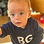 baby, child, indoor, blue_eyes, sweater, navy_clothing, curious, portrait, close_up, infant, person, young_child, cute, soft_lighting, blurry_background, expression, reaching_hand, face, head, candid