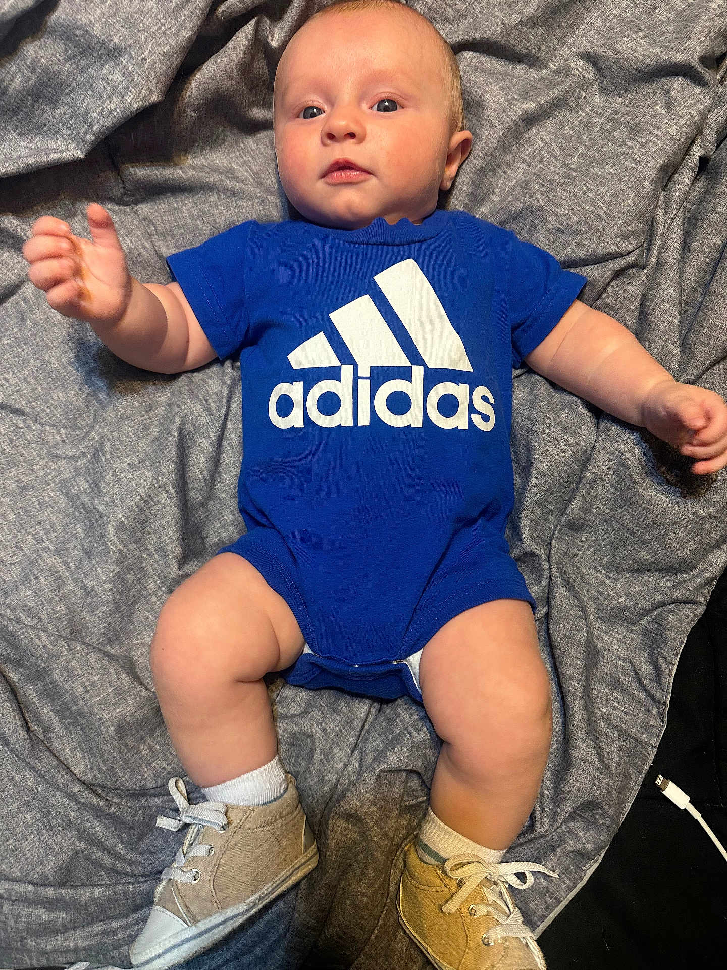 Tyler is registered to the contest to win money with this photo: baby, infant, blue_onesie, adidas, sneakers, white_socks, blanket, gray_blanket, cute, child, toddler, lying_down, indoors, clothing, footwear, person, small_shoes, soft_texture, reaching_hand, curious_expression