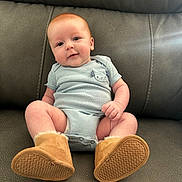 Asher joined the competition — help win amazing prizes! baby, infant, couch, blue_onesie, boots, footwear, smiling, cute, child, indoor, portrait, sitting, face, skin, head, happy, furniture, soft, warm, comfort