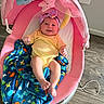 Anluisa is registered to the contest to win money with this photo: baby, infant, pink_baby_rocker, yellow_onesie, headband, blue_blanket, dinosaur_pattern, happy, smiling, indoor, wooden_floor, baby_toy, baby_accessory, child, person, cozy, relaxed, cute, playful, resting