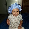 toddler, child, smiling, bonnet, pajamas, leopard_print, indoor, blanket, lamp, furniture, room, happy, person, portrait, seated, headwear, cute, young_child, cozy, home