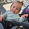 toddler, child, stroller, smile, pony_tail, face, hand, clothing, outdoor, sunlight, shadow, chair, floor, person, baby, casual, happy, daylight, seating, playful