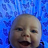 baby, blanket, blue, butterfly, child, closeup, clothing, cute, expression, eyes, face, happy, indoors, infant, lying_down, pattern, person, portrait, skin, smiling