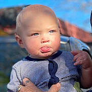 Lliam is registered to the contest to win money with this photo: baby, child, infant, person, blue_eyes, striped_clothing, tattoo, arm, hand, outdoor, sky, sunlight, tongue_out, cute, holding, portrait, young_child, expression, daylight, casual