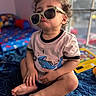 Roman is registered to the contest to win money with this photo: toddler, child, sunglasses, pout, curly_hair, bed, indoor, window, toy, blue_bedspread, shirt, casual_clothing, expression, sitting, barefoot, colorful, home, portrait, cute, funny
