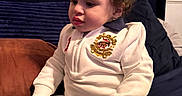 Roman is registered to the contest to win money with this photo: toddler, child, curly_hair, white_outfit, sitting, couch, blue_cushion, brown_cushion, indoor, portrait, cute, young_child, clothing, long_sleeve, pants, home, furniture, relaxed, person, expression