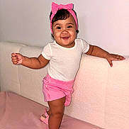 Alma is registered to the contest to win money with this photo: baby, child, smiling, portrait, indoor, couch, pink, headband, bow, shorts, sandals, clothing, sitting, standing, happy, face, hair, furniture, home, photography