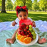 baby, child, infant, portrait, outdoor, park, picnic, blanket, fruit_cake, strawberries, grapes, oranges, fruit, red_bow, headband, white_shirt, sitting, smiling, birthday, greenery