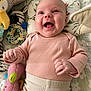 baby, infant, smiling, happy, lying_down, plush_toy, pink_clothing, cream_pants, face, child, cute, joyful, indoors, toy, soft_texture, blanket, patterned, closeup, human, playtime