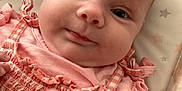 Ava is registered to the contest to win money with this photo: baby, infant, face, pink_clothing, smile, close_up, hand, eyes, cute, newborn, ruffles, blanket, pattern, skin, person, lying_down, child, apparel, adorable, expression