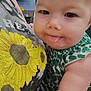 baby, child, tongue_out, close_up, infant, person, arm, clothing, pattern, sunflower, shirt, indoor, holding, face, skin, cute, expression, young, human, portrait