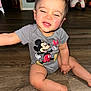 baby, child, mickey_mouse, onesie, sitting, floor, wooden_floor, funny_face, expression, indoor, toy, playroom, person, cute, infant, smiling, head, arm, leg, foot