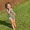 barefoot, casual, child, cute, daylight, expression, fence, grass, mickey_mouse, nature, onesie, outdoor, person, playful, portrait, standing, summer, sunlight, toddler, young_child