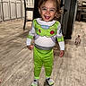 Colton is registered to the contest to win money with this photo: buzz_lightyear_costume, casual, chairs, child, clothing, face, green_pants, happy, home, indoor, kitchen, person, smiling, socks, standing, table, toddler, toy, wooden_floor, young_child