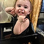 toddler, child, smile, happy, high_chair, black_clothing, indoor, wood_paneling, cushioned_chair, person, face, cute, playful, baby, earrings, skin, furniture, window, expression, portrait