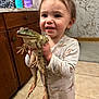 toddler, child, frog, animal, pajamas, smile, indoor, kitchen, tile_floor, wooden_cabinets, person, holding, cute, happy, face, young_child, bathroom_products, marble_wall, floor, curly_hair