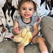 Wren is registered to the contest to win money with this photo: toddler, child, smiling, plush_toy, pink_bow, striped_shirt, shorts, socks, couch, blanket, horse_pattern, indoors, happy, person, portrait, cute, young_child, seated, home, comfort
