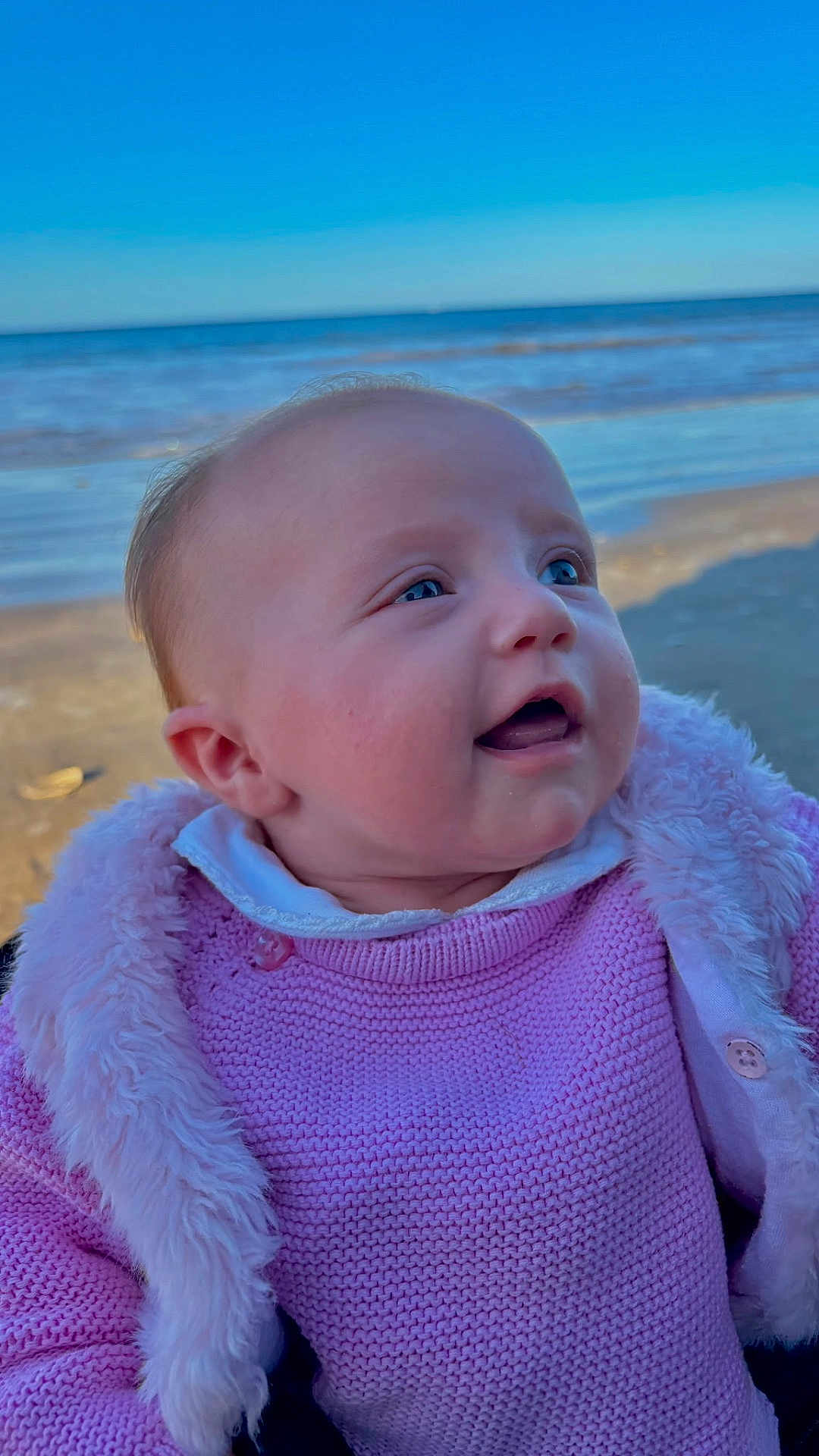 Noélie a rejoint le concours — aidez-le/la à gagner de superbes lots ! baby, infant, child, beach, ocean, sea, water, sky, horizon, sand, portrait, close_up, face, smiling, happy, pink_sweater, fur_trim, outdoor, clothing, eyes