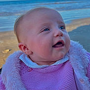 Noélie a rejoint le concours — aidez-le/la à gagner de superbes lots ! baby, infant, child, beach, ocean, sea, water, sky, horizon, sand, portrait, close_up, face, smiling, happy, pink_sweater, fur_trim, outdoor, clothing, eyes