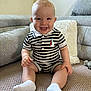 baby, child, smiling, striped_clothing, socks, sitting, indoor, couch, pillow, blanket, happy, person, face, cute, infant, furniture, home, comfort, portrait, toddler