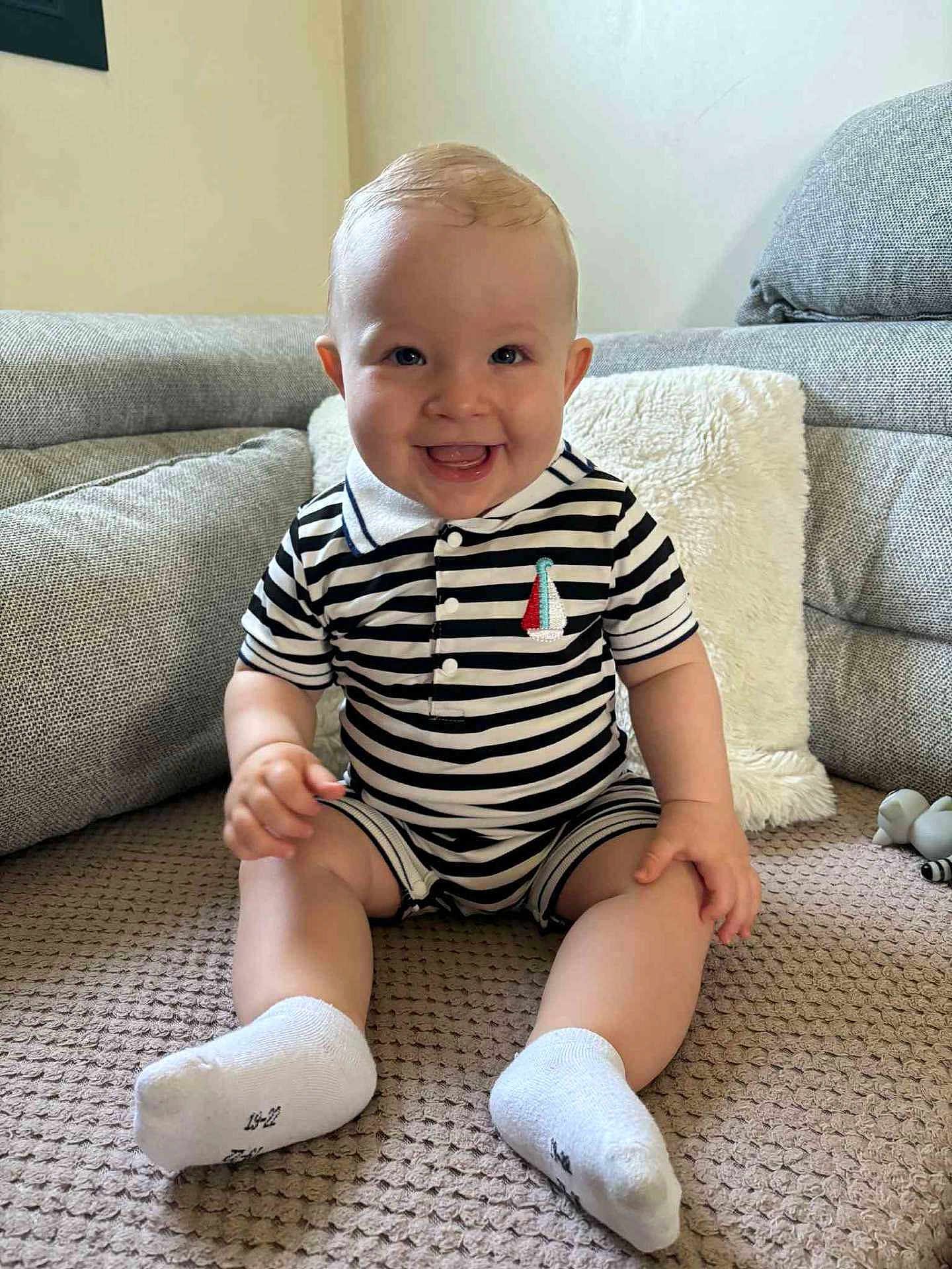 Marin participe au concours pour gagner de l'argent avec cette photo : baby, child, smiling, striped_clothing, socks, sitting, indoor, couch, pillow, blanket, happy, person, face, cute, infant, furniture, home, comfort, portrait, toddler