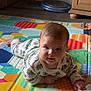baby, child, pajamas, playmat, colorful, indoor, floor, wooden_cabinet, toy, pattern, curious, lying_down, cheeks, face, infant, cute, home, soft_lighting, person, young_child