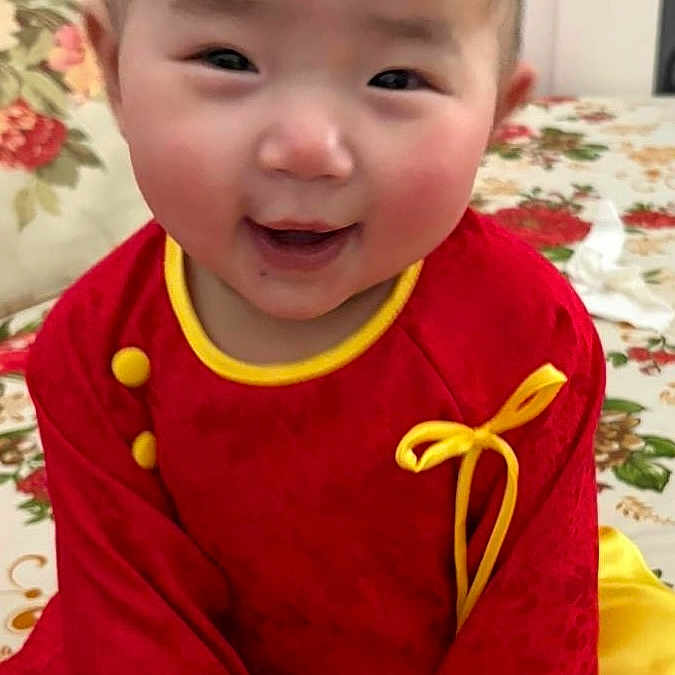Luana is registered to the contest to win money with this photo: baby, bedroom, child, closeup, cute, door, door_knob, eyes, fabric, floral_bedspread, hands, happy, indoor, portrait, red_outfit, rosy_cheeks, short_hair, sitting, smile, yellow_trim