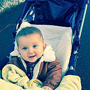 Coman participe au concours pour gagner de l'argent avec cette photo : baby, child, stroller, blanket, jacket, smile, outdoor, pavement, happy, face, person, warm_clothing, cozy, blue_eyes, infant, cute, baby_clothes, childhood, seat, transport