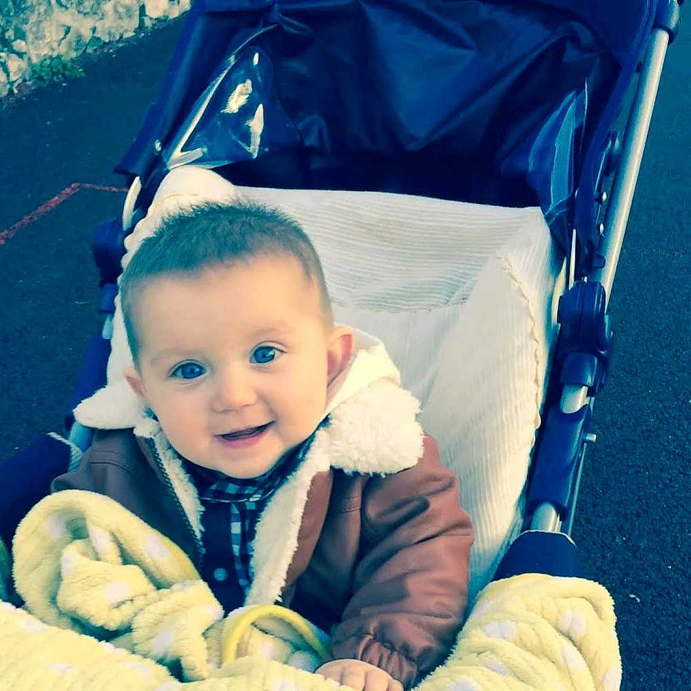 Coman participe au concours pour gagner de l'argent avec cette photo : baby, baby_clothes, blanket, blue_eyes, child, childhood, cozy, cute, face, happy, infant, jacket, outdoor, pavement, person, seat, smile, stroller, transport, warm_clothing