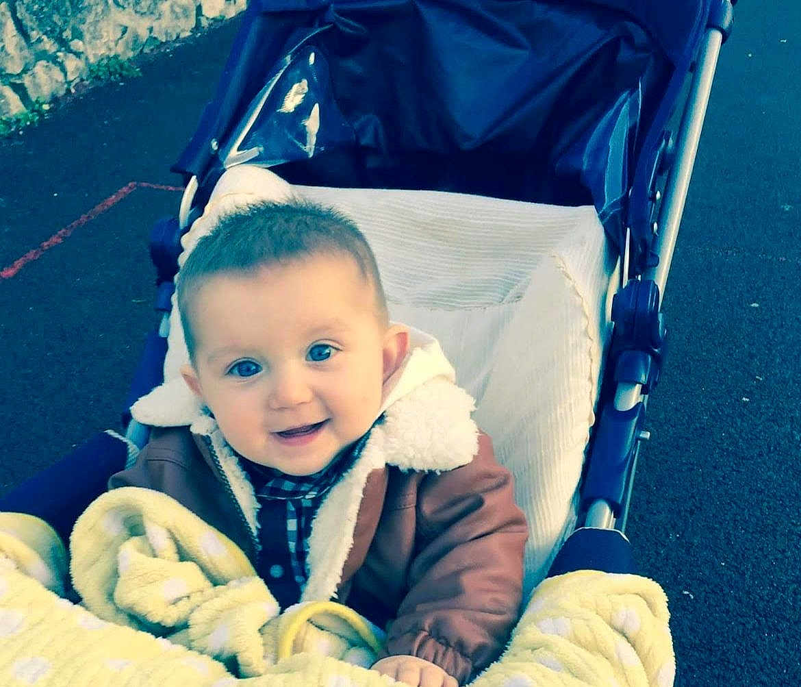 Coman participe au concours pour gagner de l'argent avec cette photo : baby, child, stroller, blanket, jacket, smile, outdoor, pavement, happy, face, person, warm_clothing, cozy, blue_eyes, infant, cute, baby_clothes, childhood, seat, transport