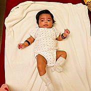 Anna is registered to the contest to win money with this photo: baby, blanket, bracelets, child, cute, expression, face, hair, indoors, infant, lying_down, newborn, person, polka_dot, red_background, resting, skin, socks, soft_texture, white_clothing