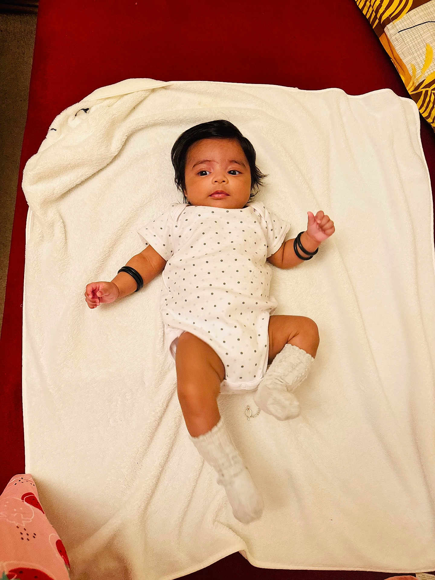 Anna is registered to the contest to win money with this photo: baby, blanket, bracelets, child, cute, expression, face, hair, indoors, infant, lying_down, newborn, person, polka_dot, red_background, resting, skin, socks, soft_texture, white_clothing