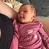 apple_pattern, arm, baby, blanket, child, couch, cute, fabric, face, happy, home_interior, indoors, infant, person, pink_clothing, portrait, seated, skin, smiling, soft_toys